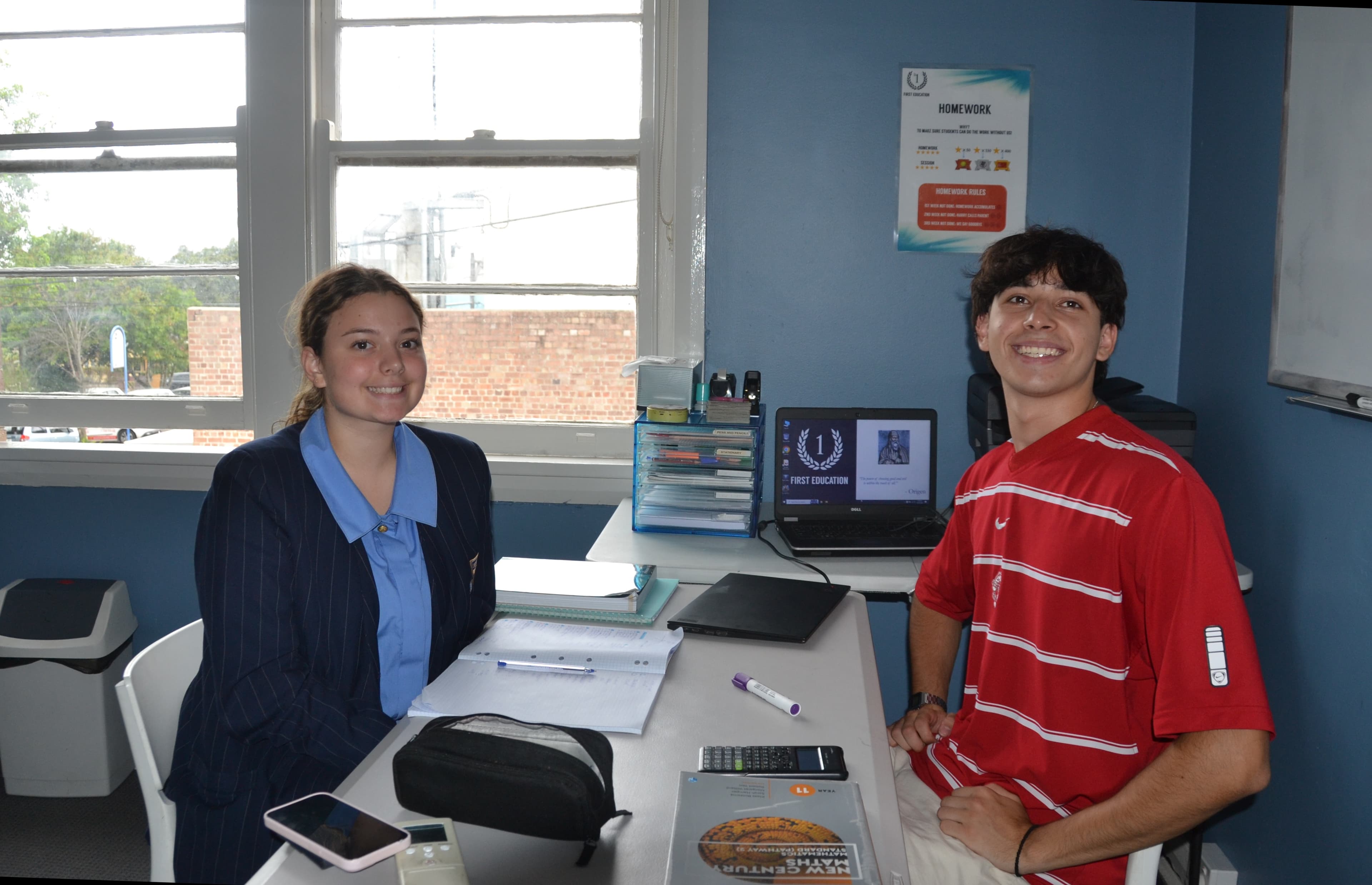 A First Education tutor and a student sitting together at a centre desk with worksheets and study materials.