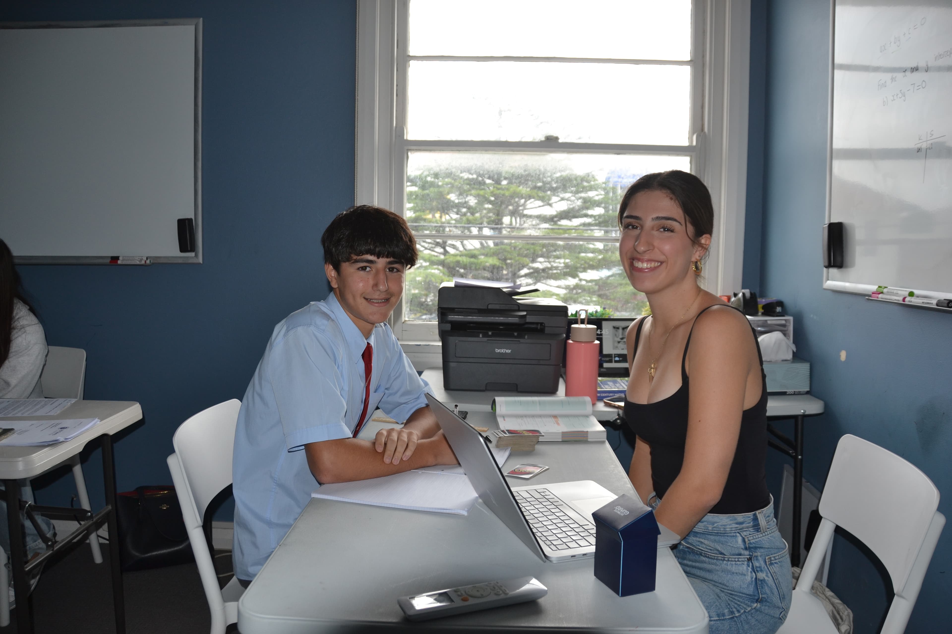 A First Education tutor and a student in school uniform sitting together at a centre desk with an open laptop and folders.