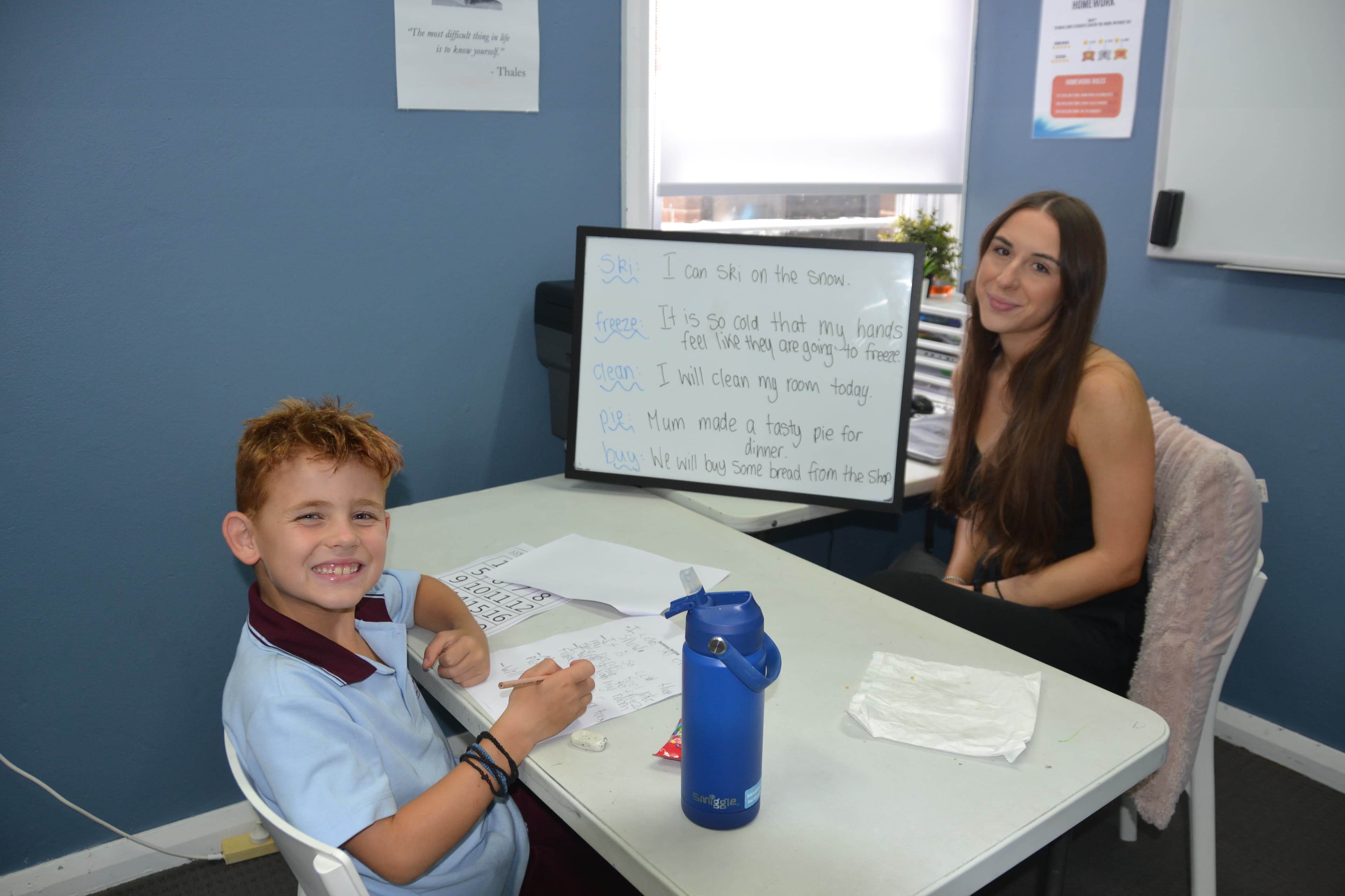 A First Education tutor and a Year 1 student sitting together at a centre desk with worksheets and study materials.