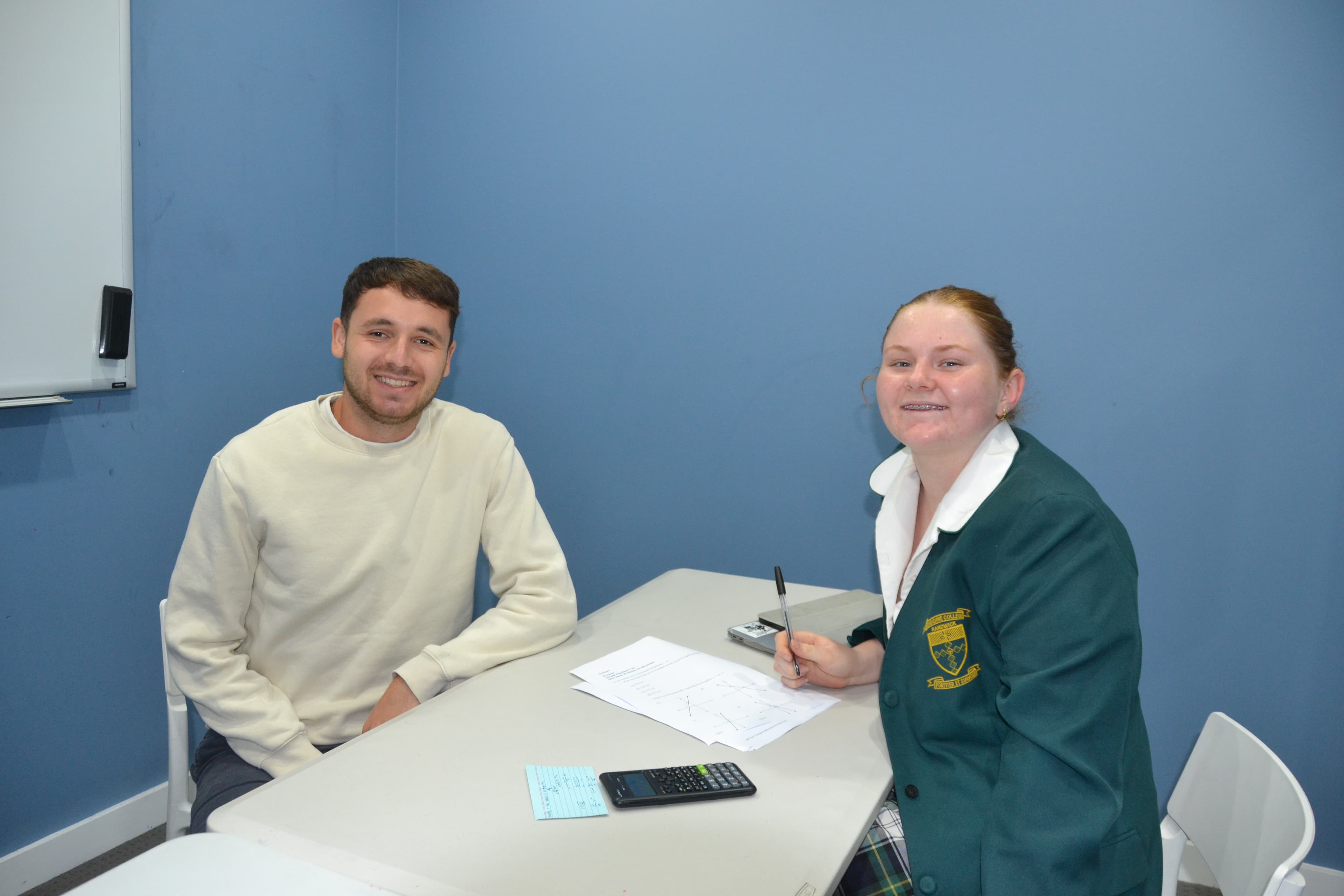 A First Education tutor and a Year 10 student in school uniform reviewing worked maths problems together at a centre desk.