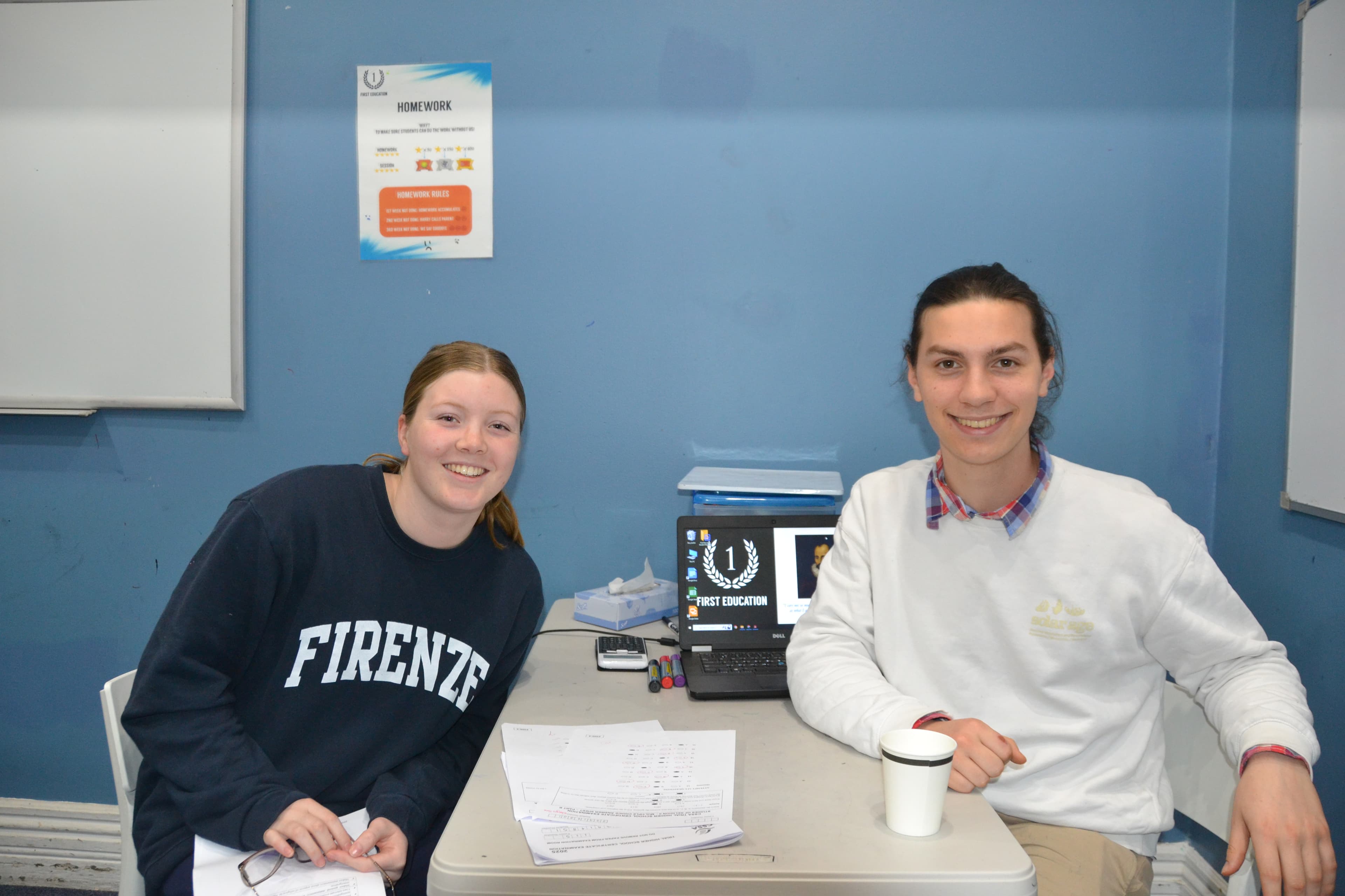 A First Education tutor and a Year 11 student sitting together at a centre desk with open workbooks and a coffee cup.