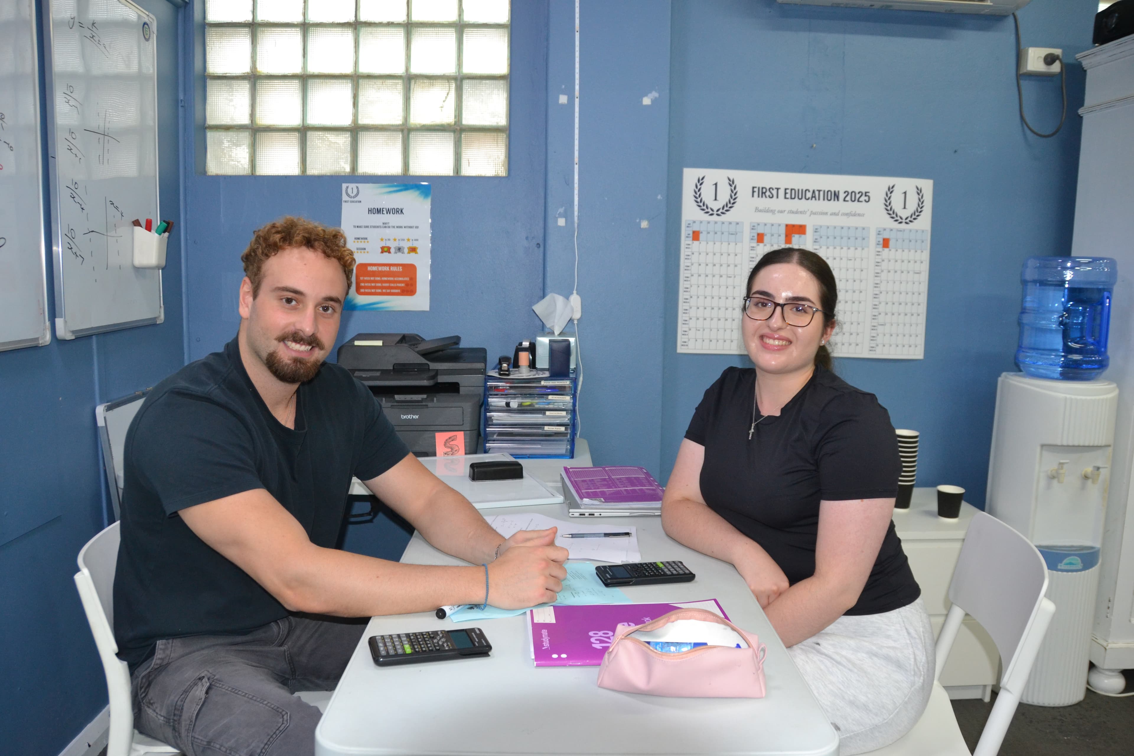 A First Education tutor and a Year 12 student giving a high five at a centre desk with worksheets and a laptop.