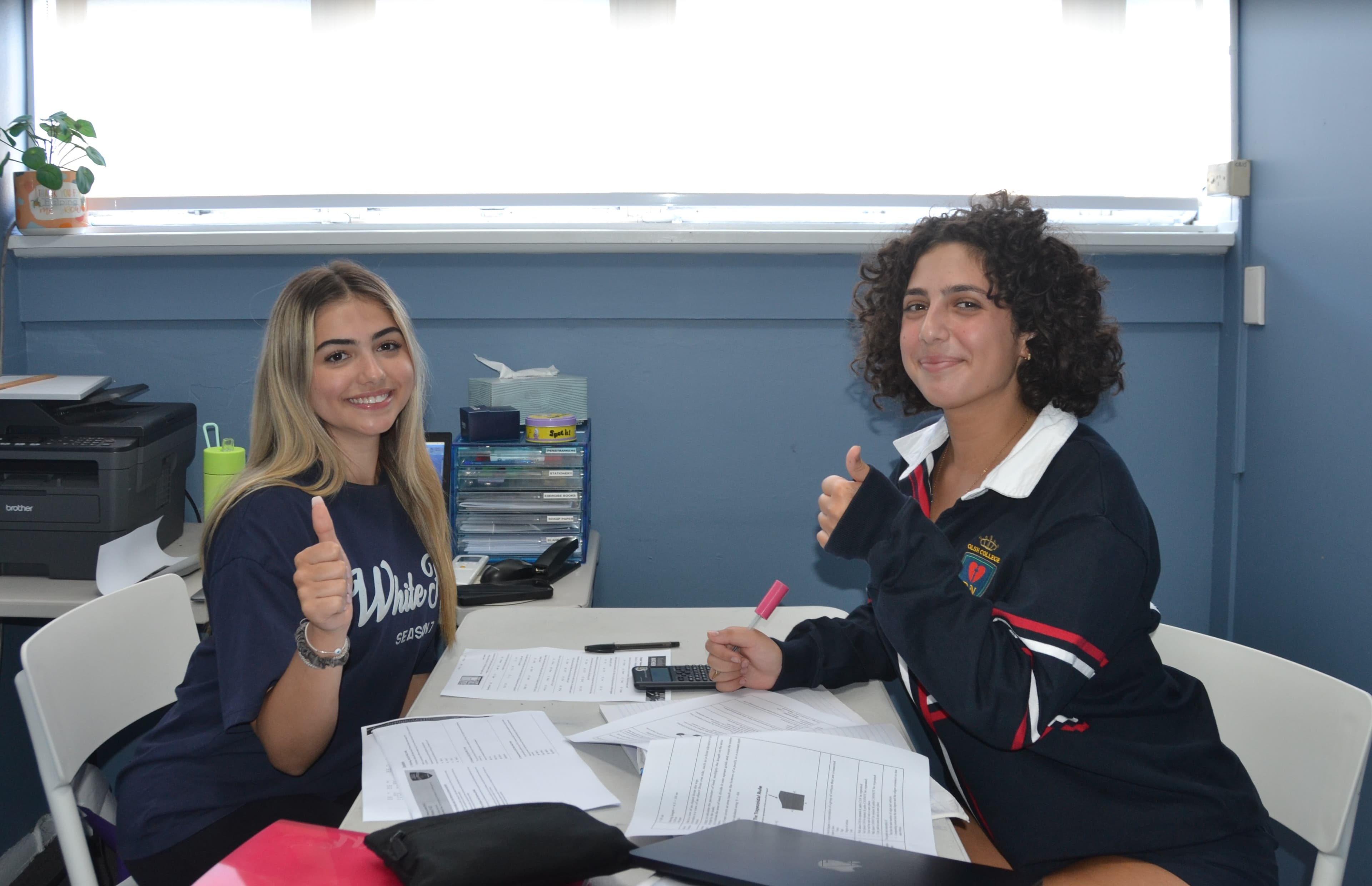A First Education tutor and a Year 12 student sitting together at a centre desk with worksheets and study materials.