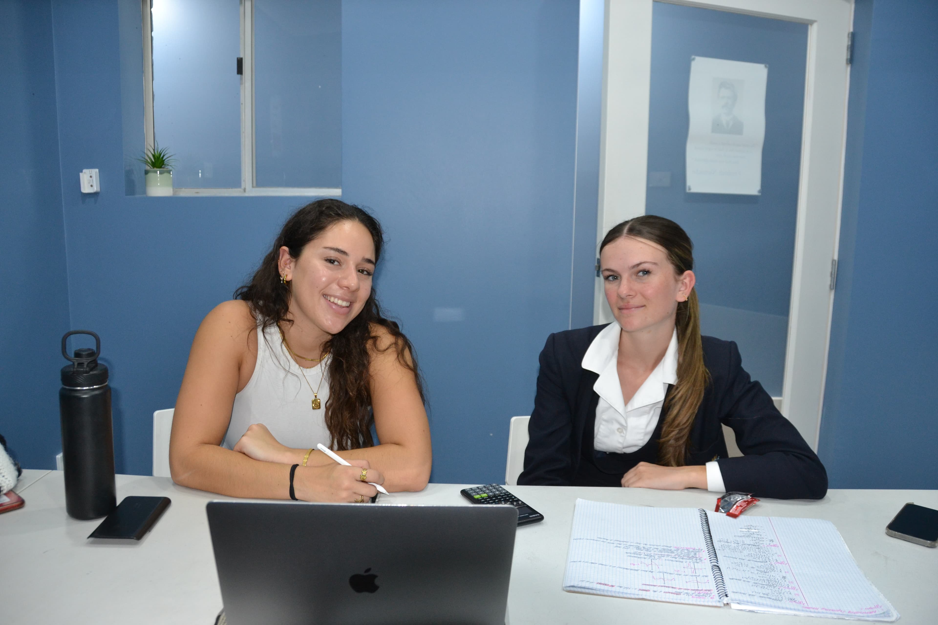 A First Education tutor and a student in school uniform giving double thumbs up at a centre desk with worksheets and a laptop.