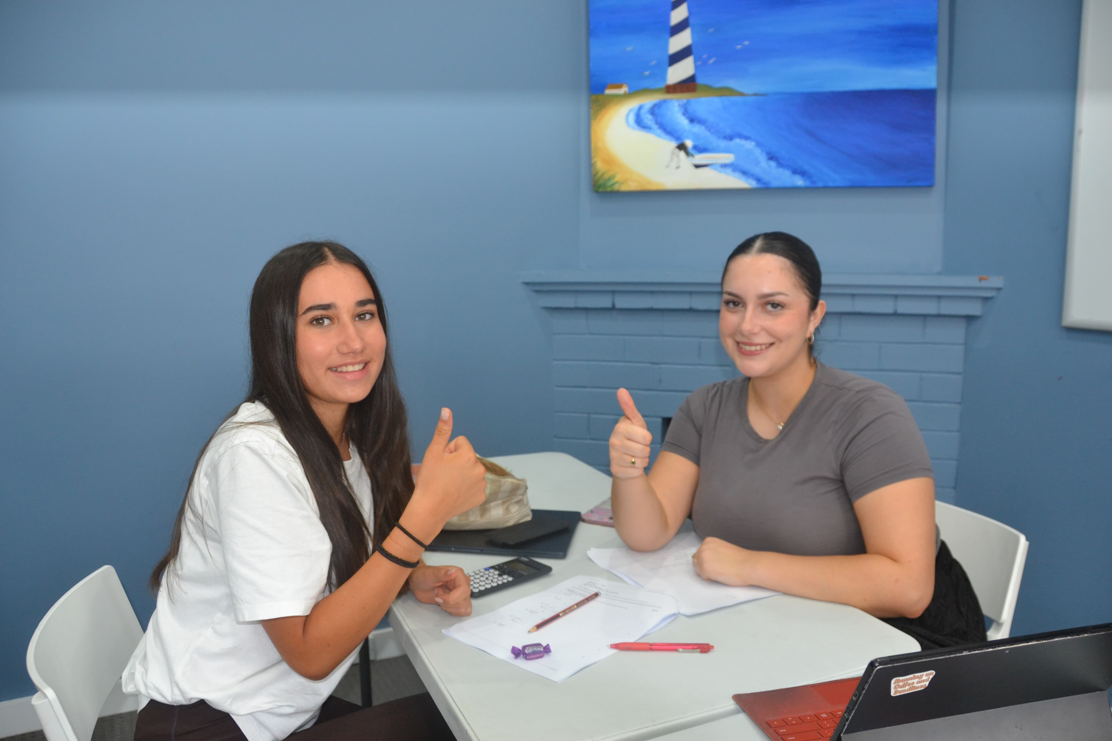 A First Education tutor and a student giving double thumbs up at a centre desk with papers and a calculator.