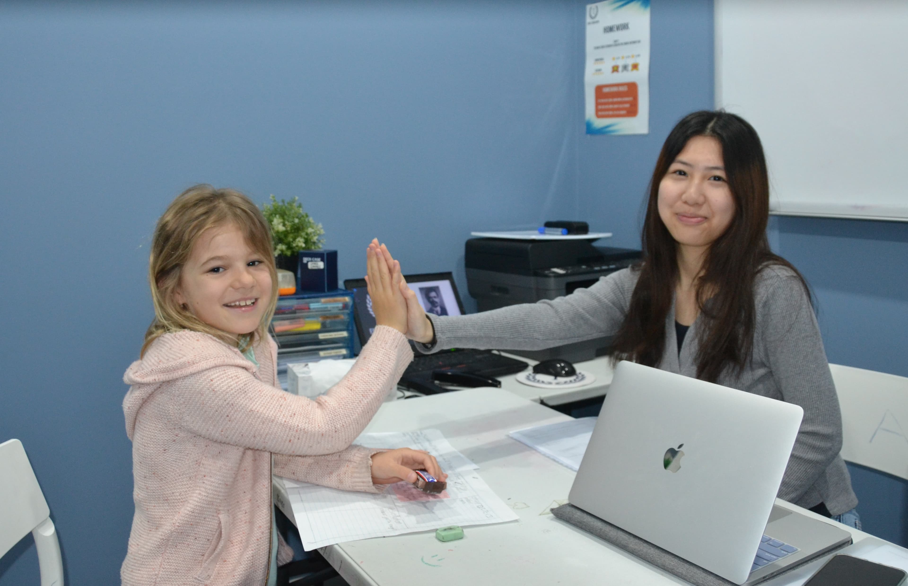 A First Education tutor and a Year 3 student sitting together at a centre desk with worksheets and study materials.