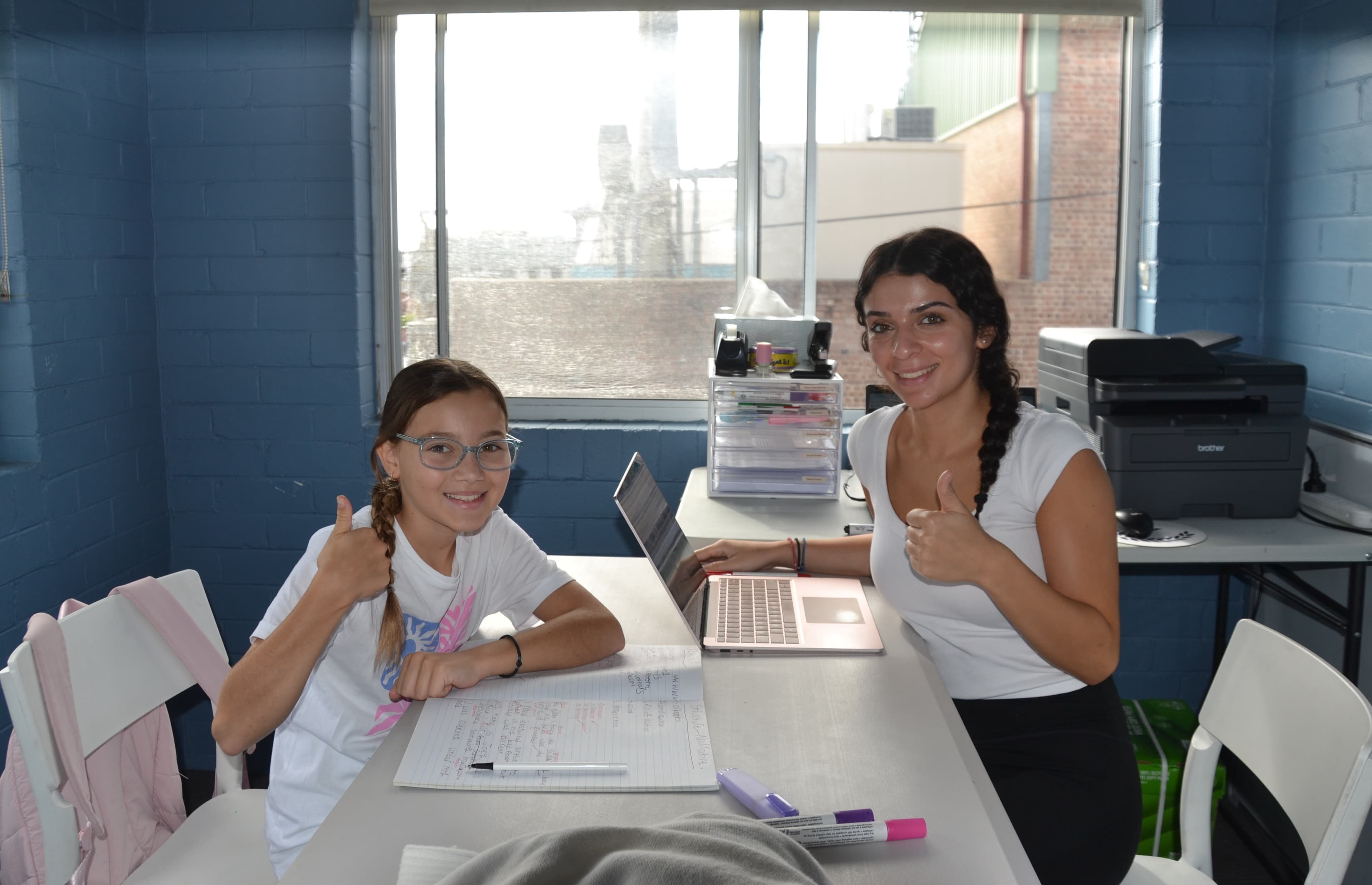 A First Education tutor and a Year 3 student giving a high five at a centre desk with open workbooks and a laptop.