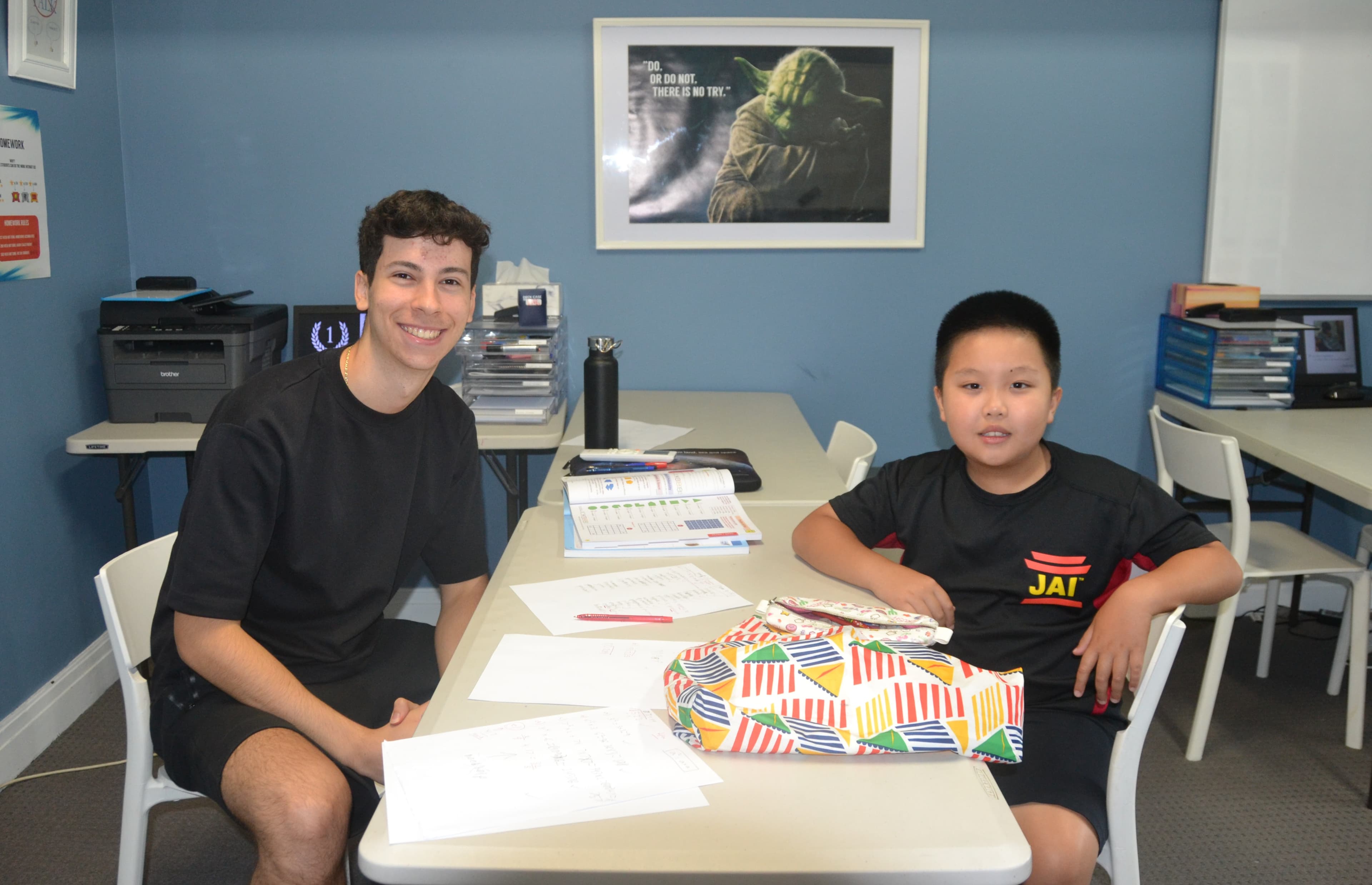 A First Education tutor and a Year 3 student sitting together at a centre desk with worksheets and a laptop.