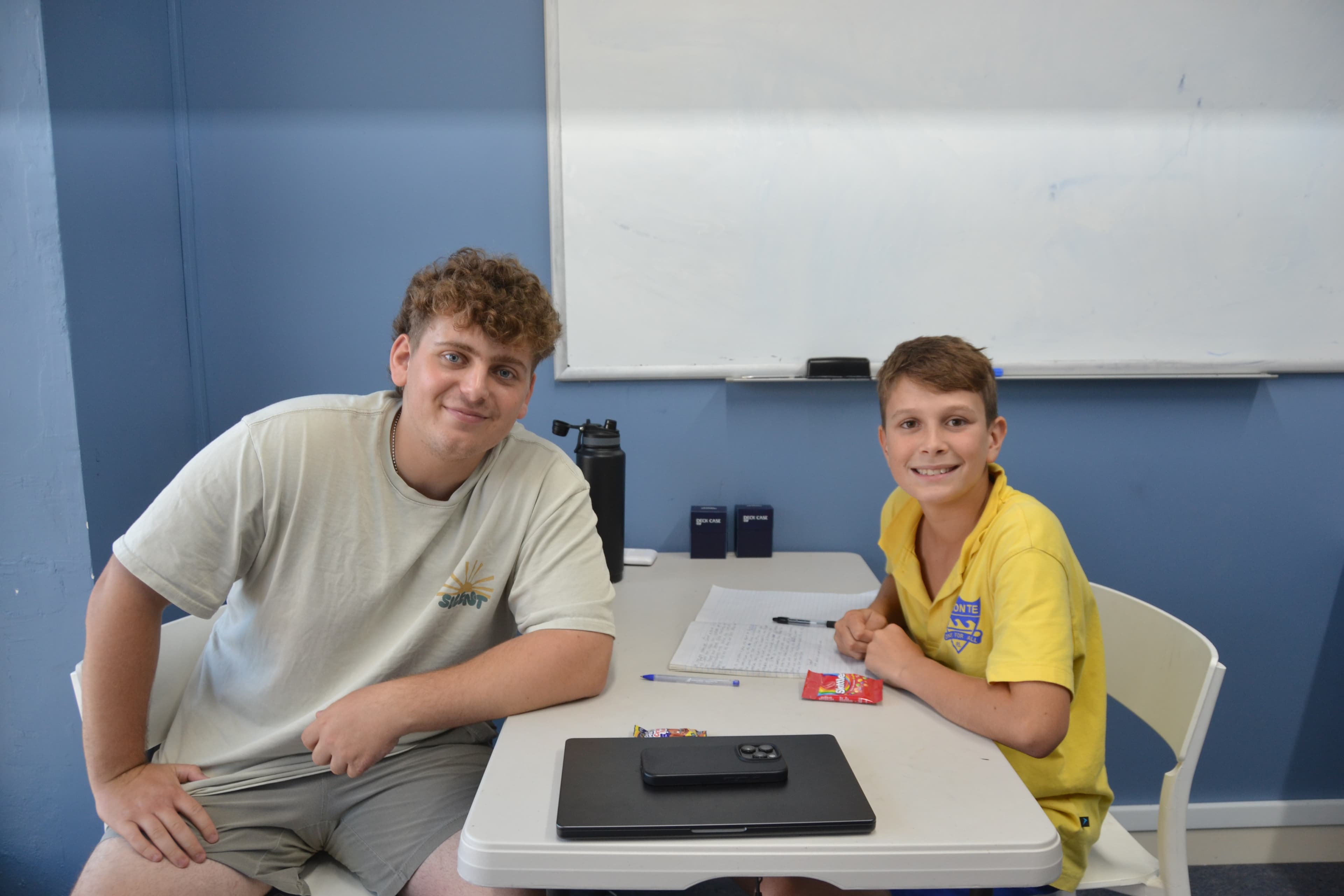 A First Education tutor and a Year 4 student in school uniform giving double thumbs up at a centre desk with open workbooks.