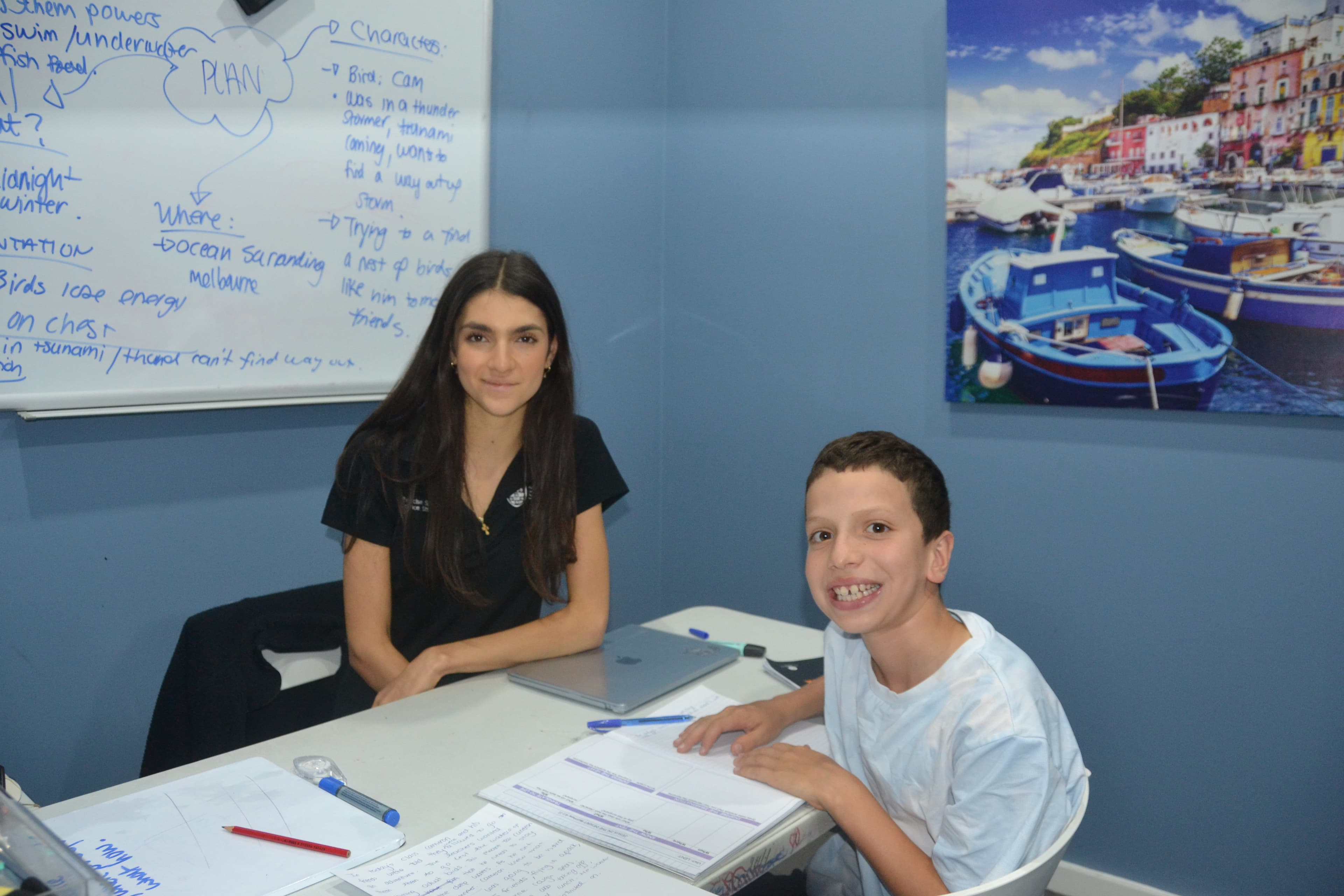 A First Education tutor and a Year 6 student sitting together at a centre desk with open worksheets and study materials.