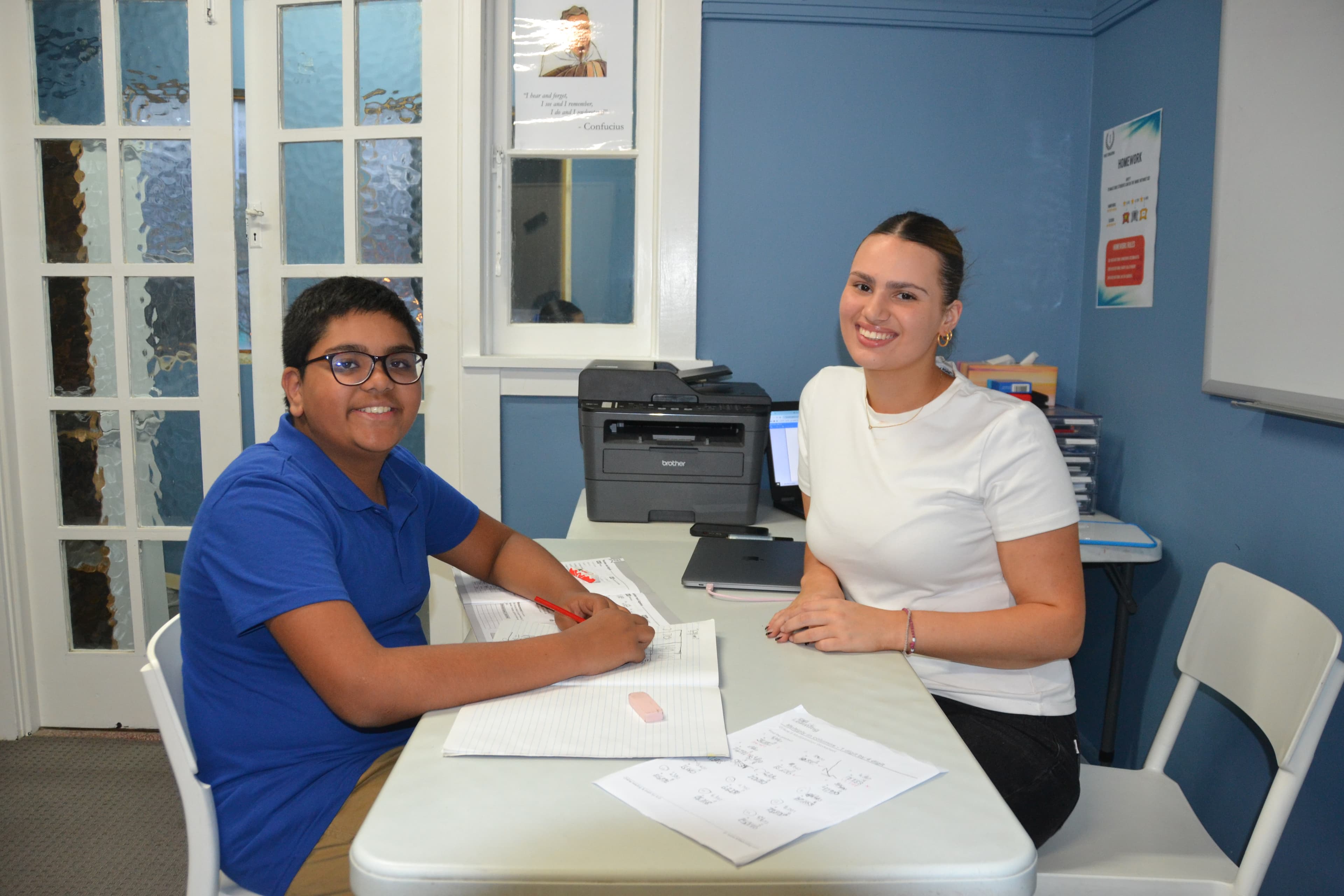 A First Education tutor and a Year 6 student giving a high five at a centre desk with open workbooks and a laptop.