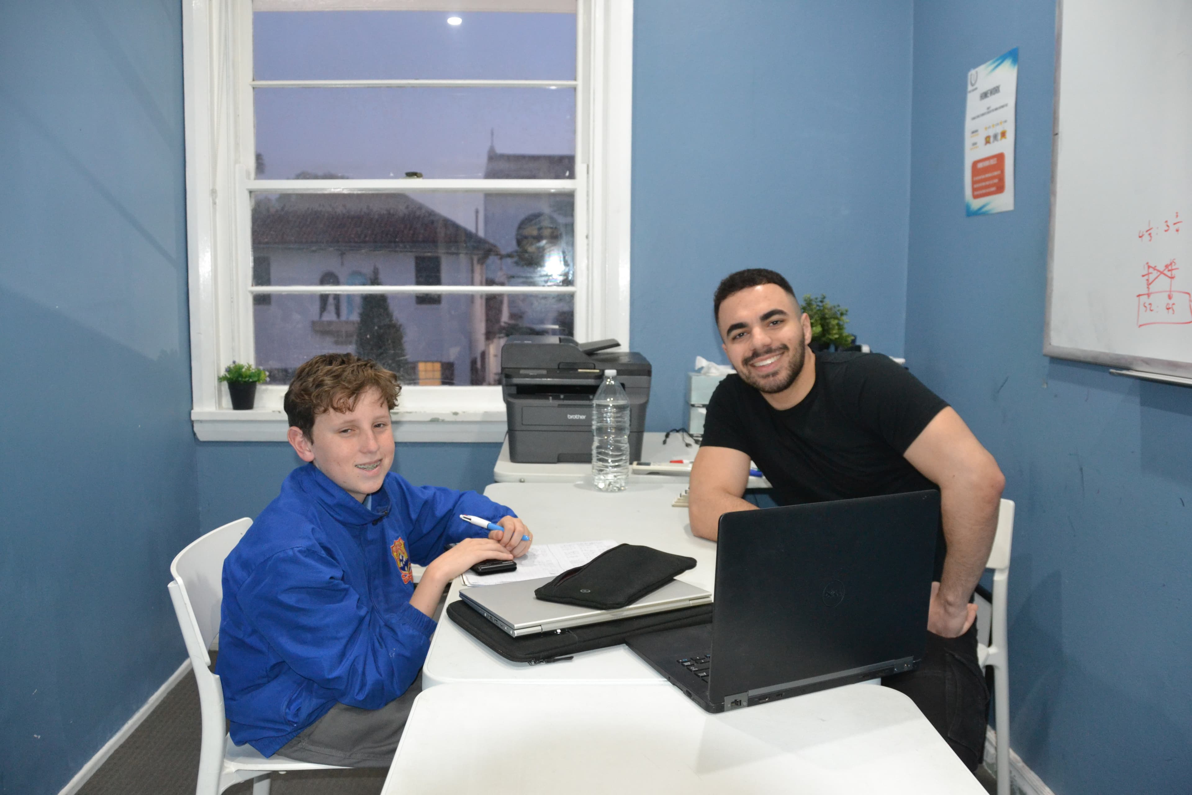 A First Education tutor and a Year 6 student sitting together at a centre desk with worksheets and a laptop.