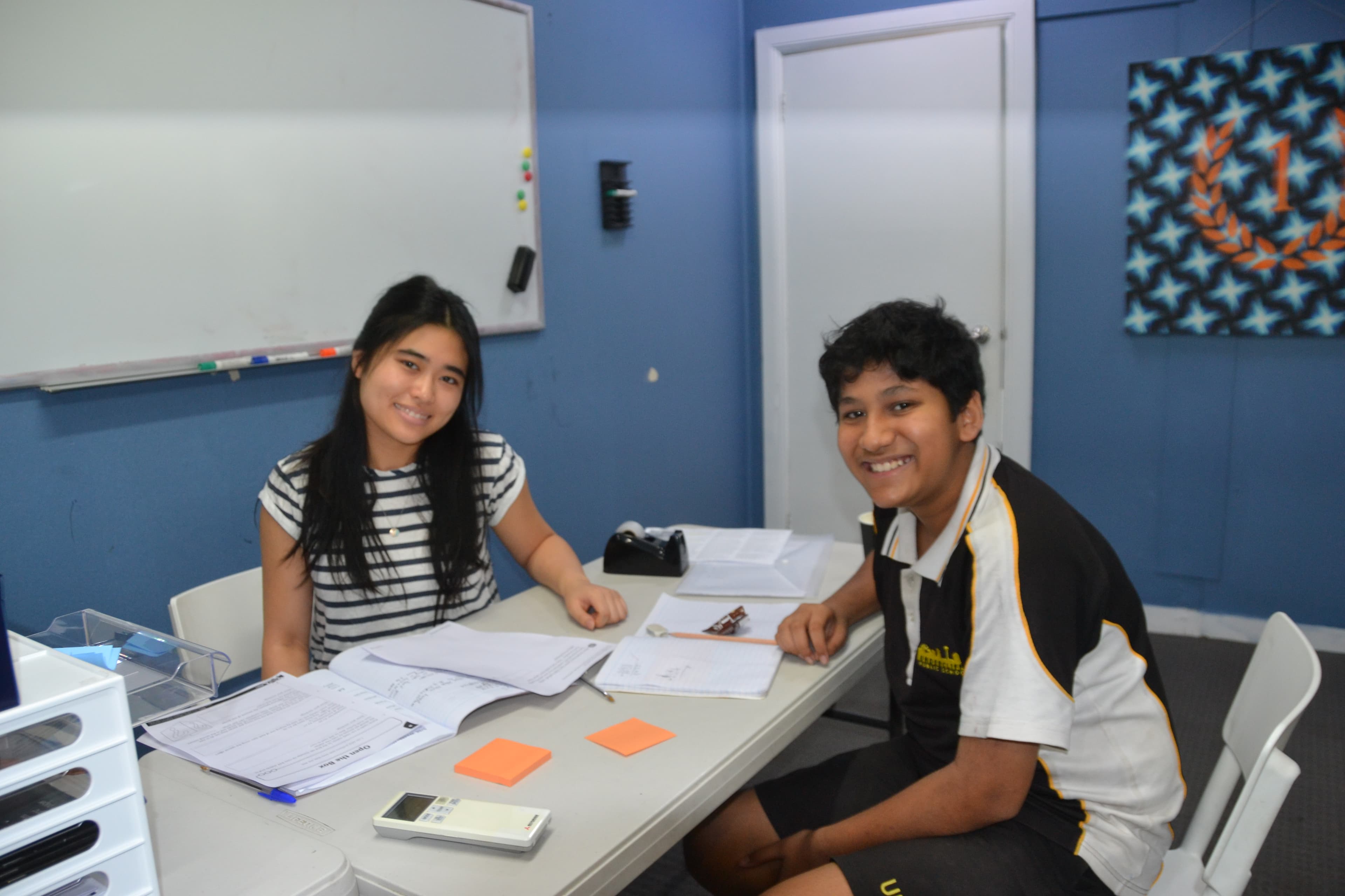 A First Education tutor and a Year 7 student sitting together at a centre desk with open workbooks and study materials.