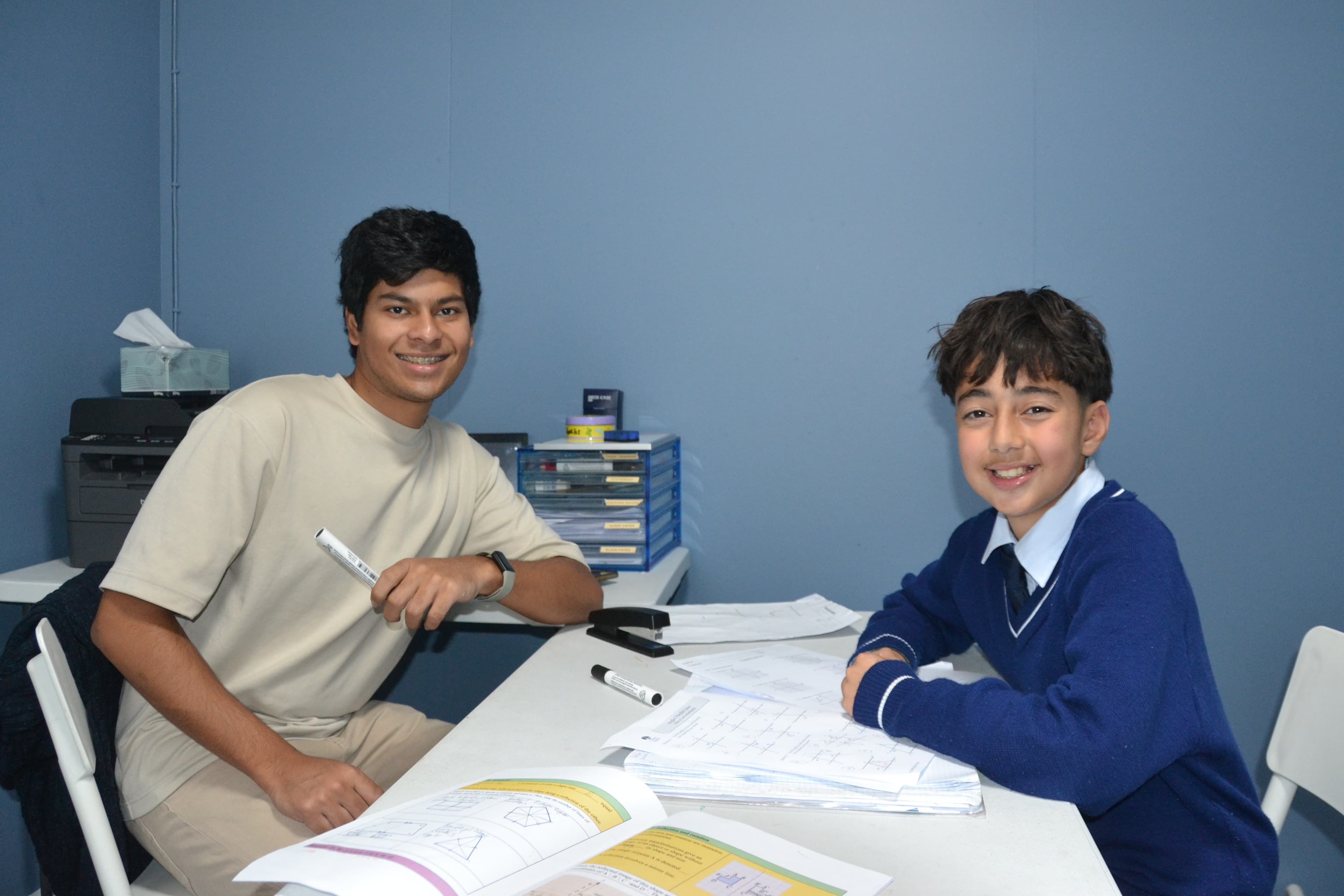 A First Education tutor and a Year 7 student sitting together at a centre desk with worksheets and a laptop.
