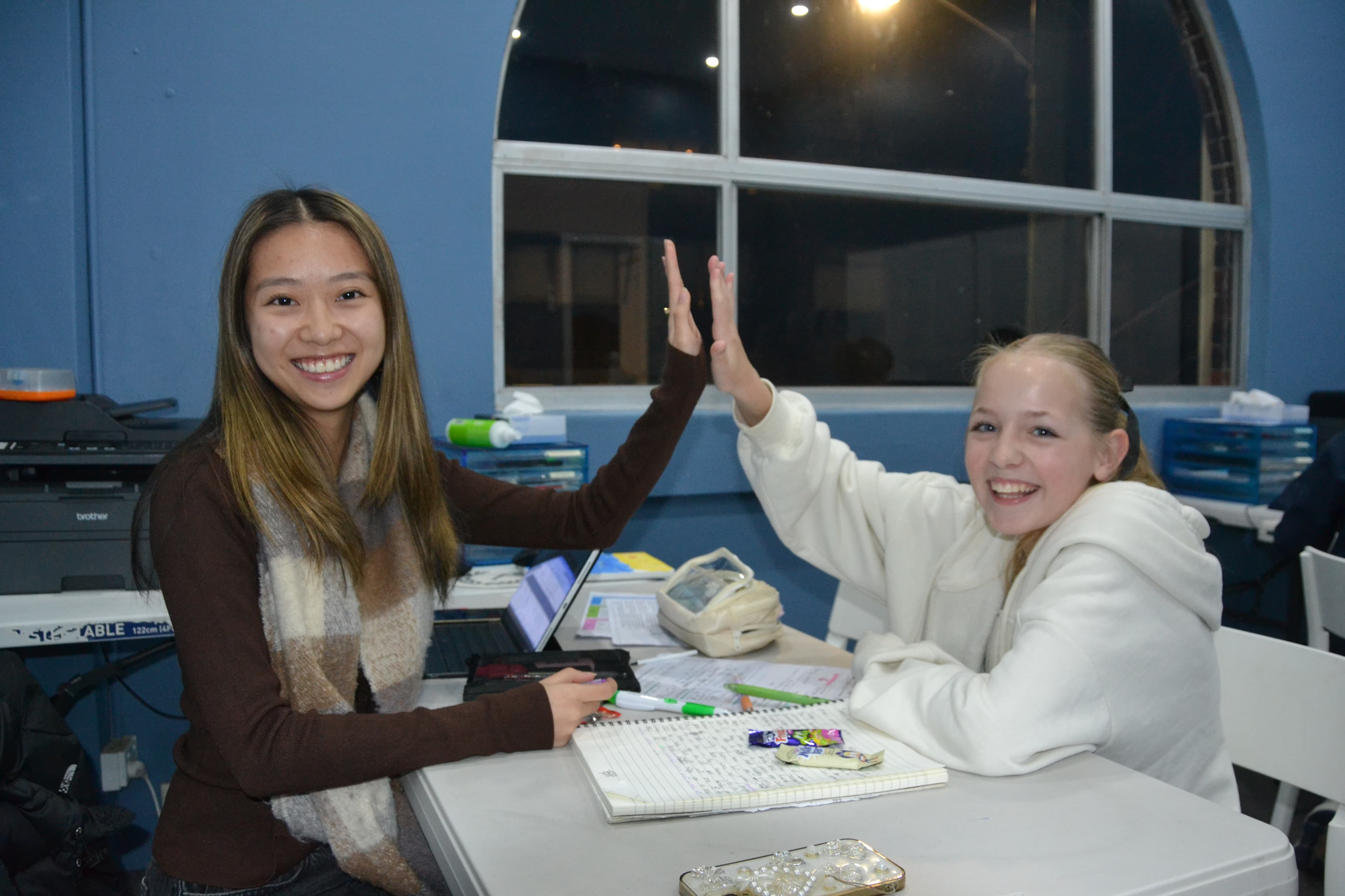 A First Education tutor and a Year 8 student sitting together at a centre desk with worksheets and a laptop.