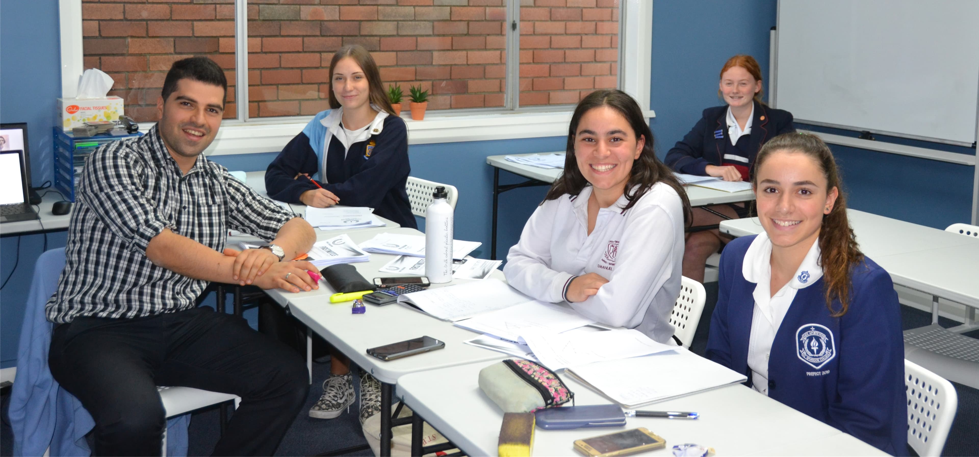 A First Education tutor and HSC students in school uniform working through past papers together at a group session.