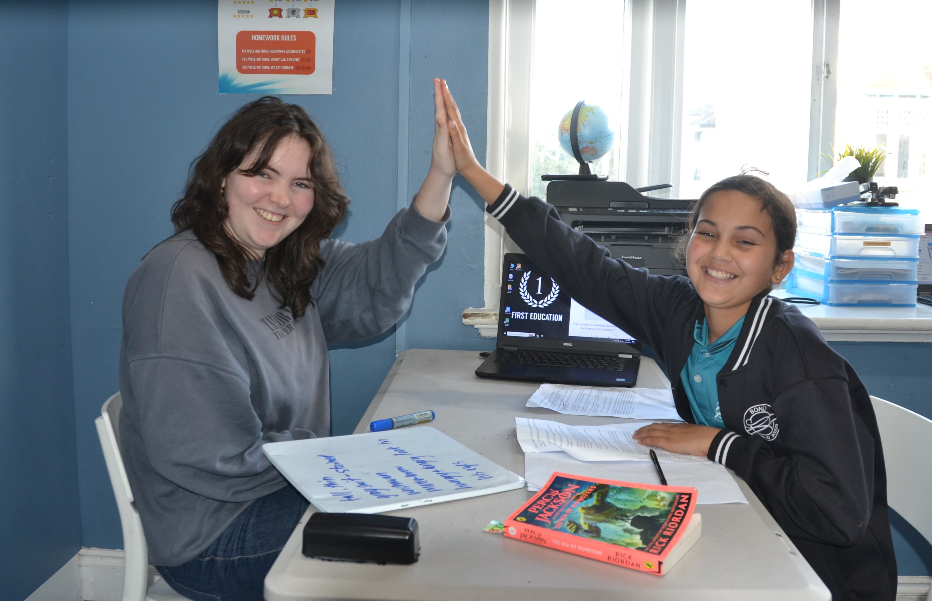 A First Education tutor and a Year 5 student sitting together at a centre desk with worksheets and study materials.