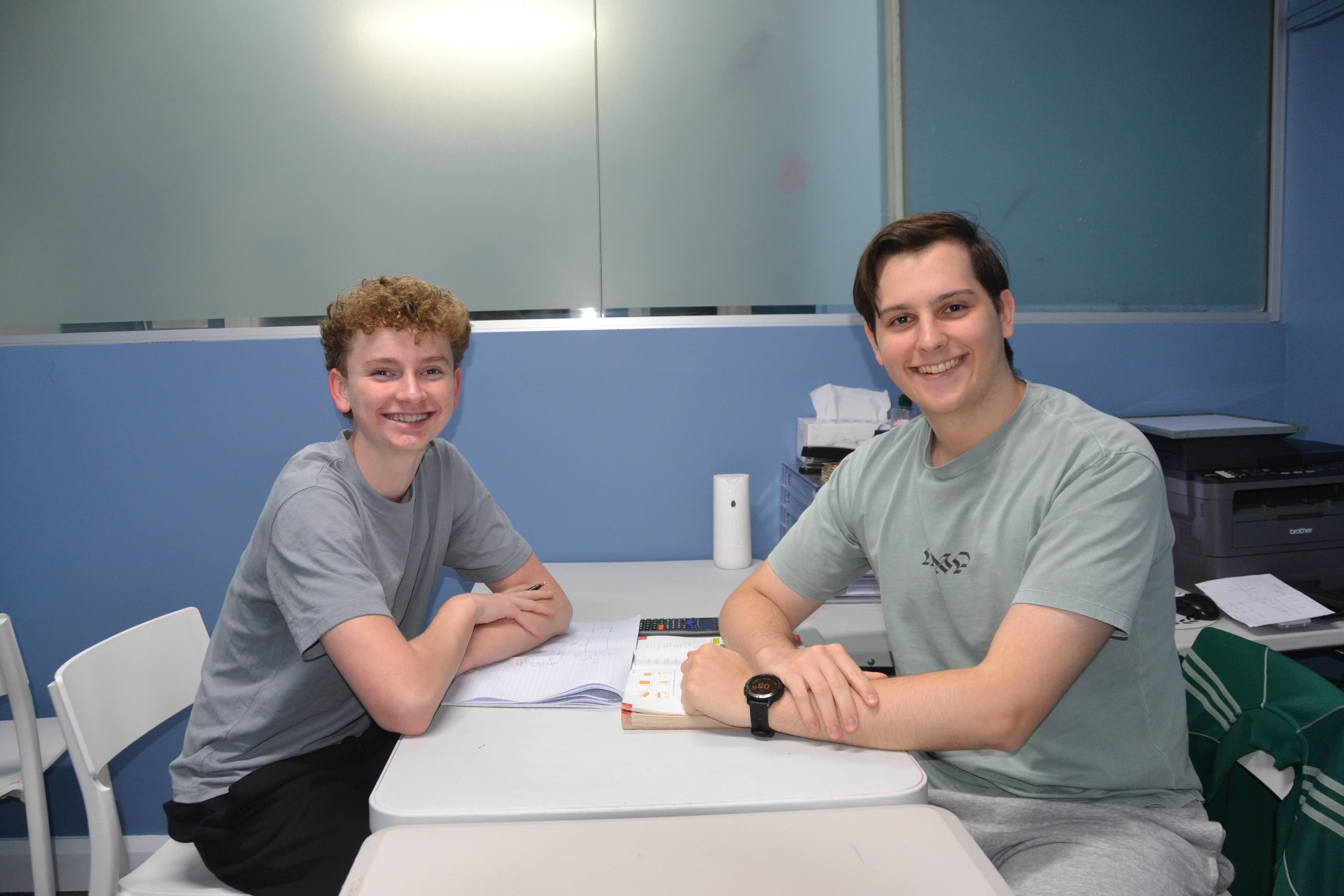 A First Education tutor and a Year 9 student sitting together at a centre desk with open worksheets and study materials.