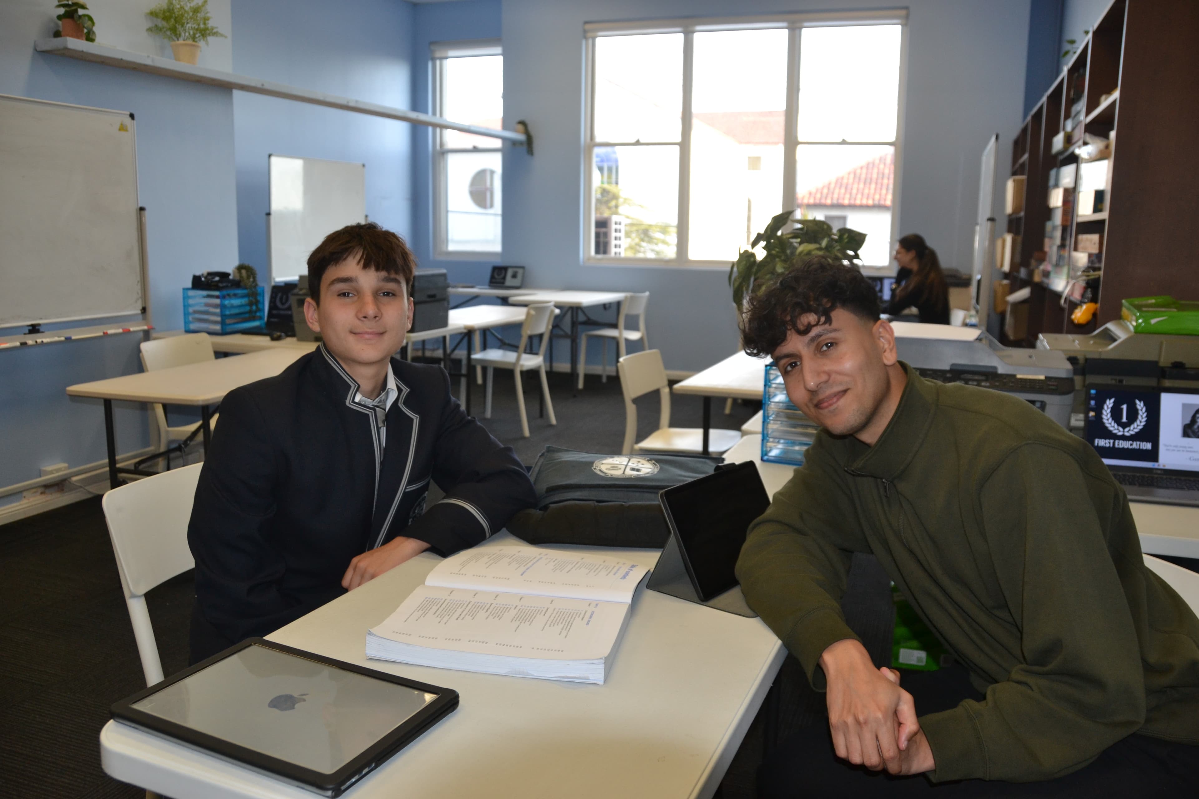 A First Education tutor and a Year 9 student sitting together at a centre desk with worksheets and a laptop.