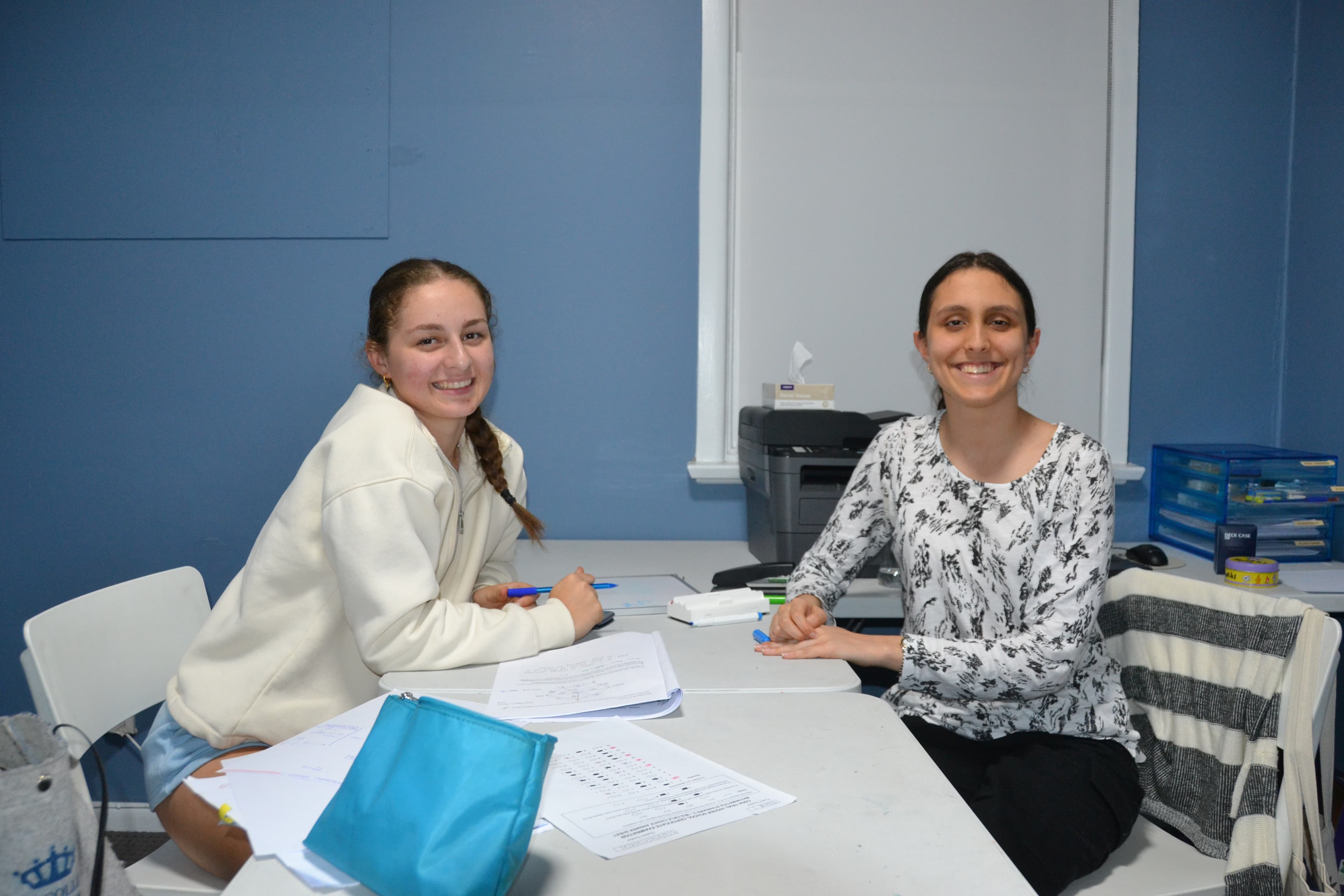 A First Education tutor and a Year 9 student sitting together at a centre desk with worksheets and study notes.